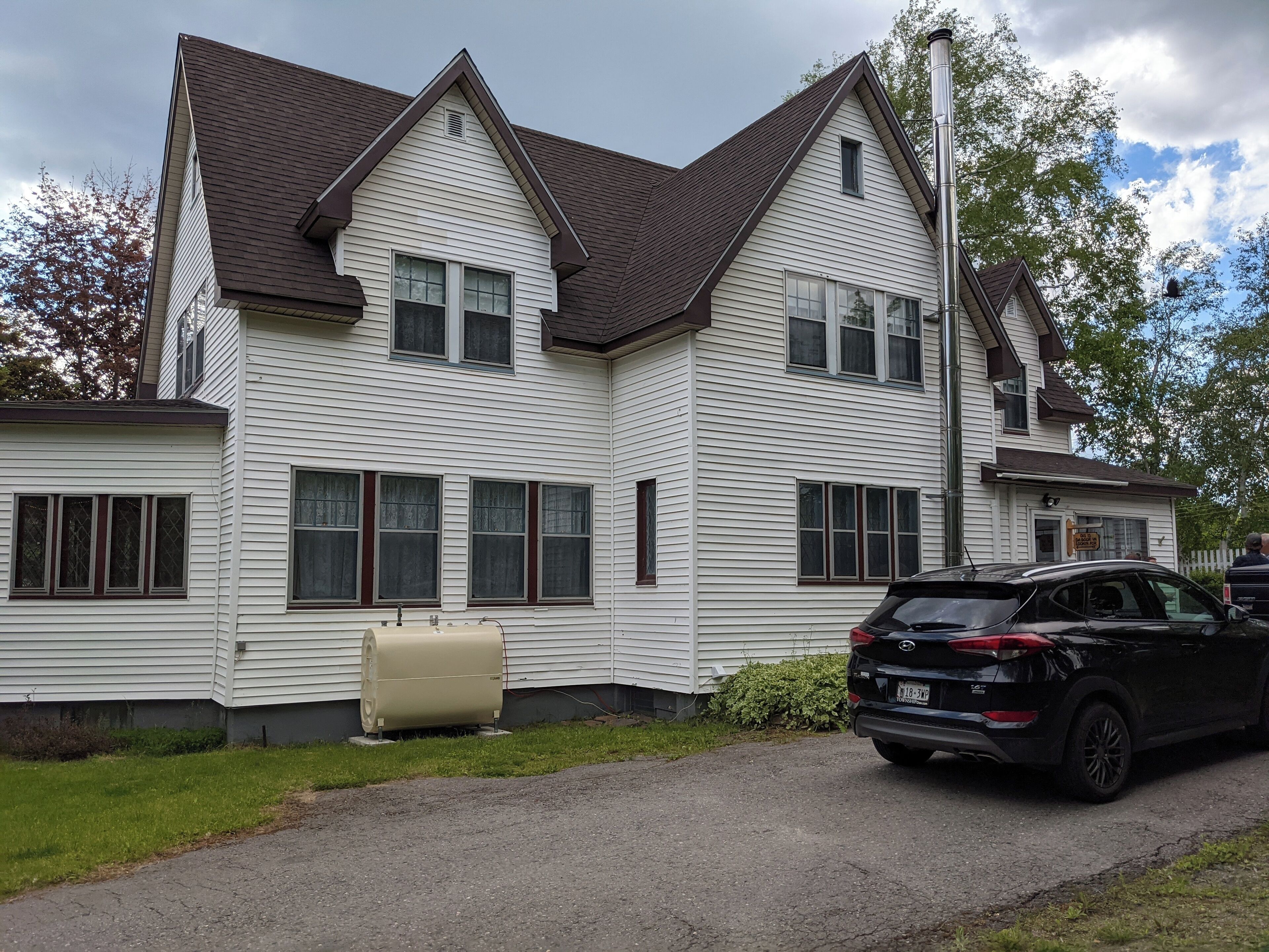A two-story house with a central chimney, a beige water heater, and a black SUV parked in front.
