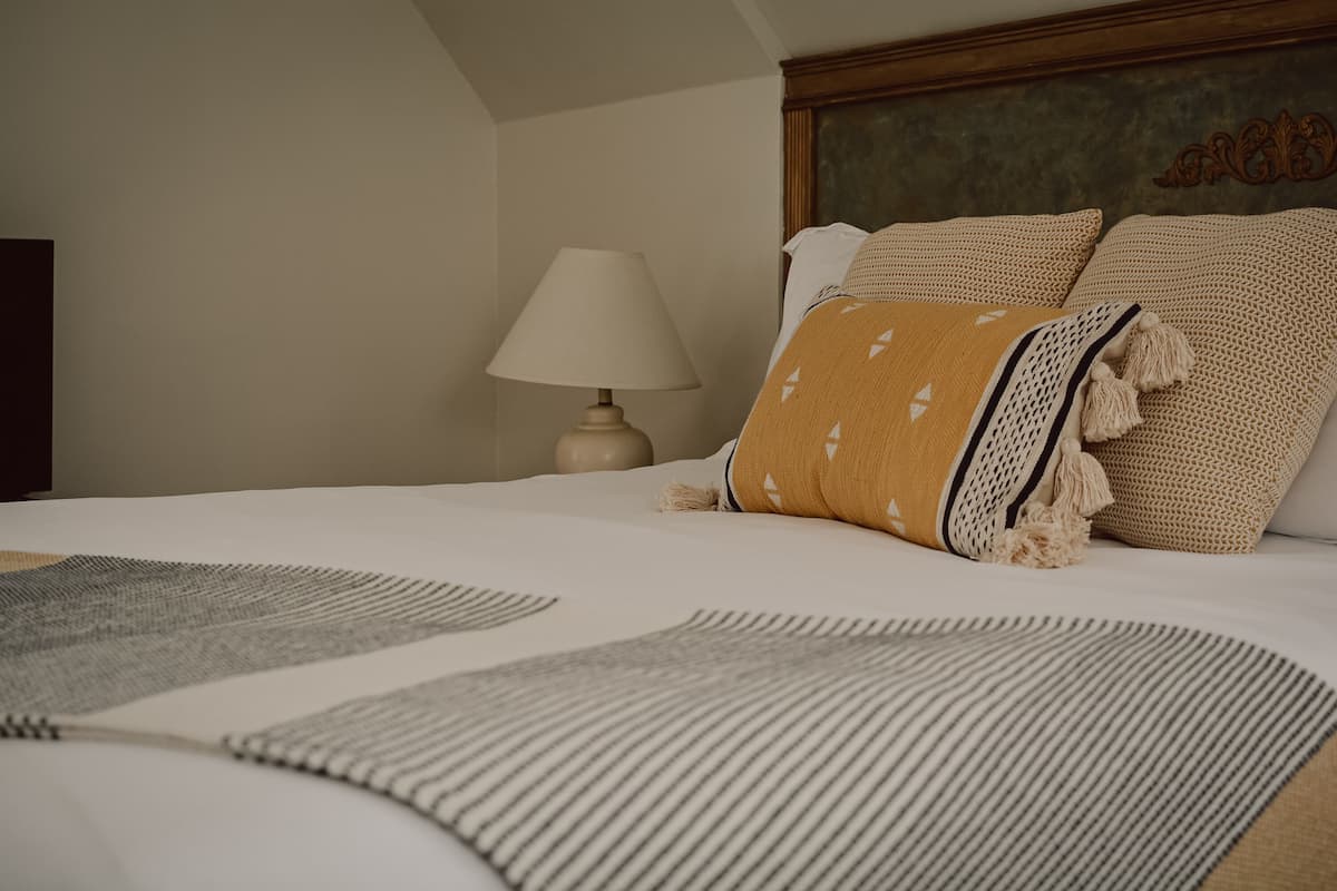 Una cama bien hecha con un plaid a rayas, una lámpara y un cabecero con diseño decorativo.