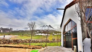 Un edificio de paredes de piedra con un amplio ventanal, un camino de piedra y vistas a montañas nevadas.