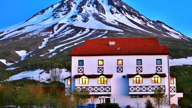 Un edificio de dos pisos con techo rojo y numerosas ventanas, frente a una montaña nevada.
