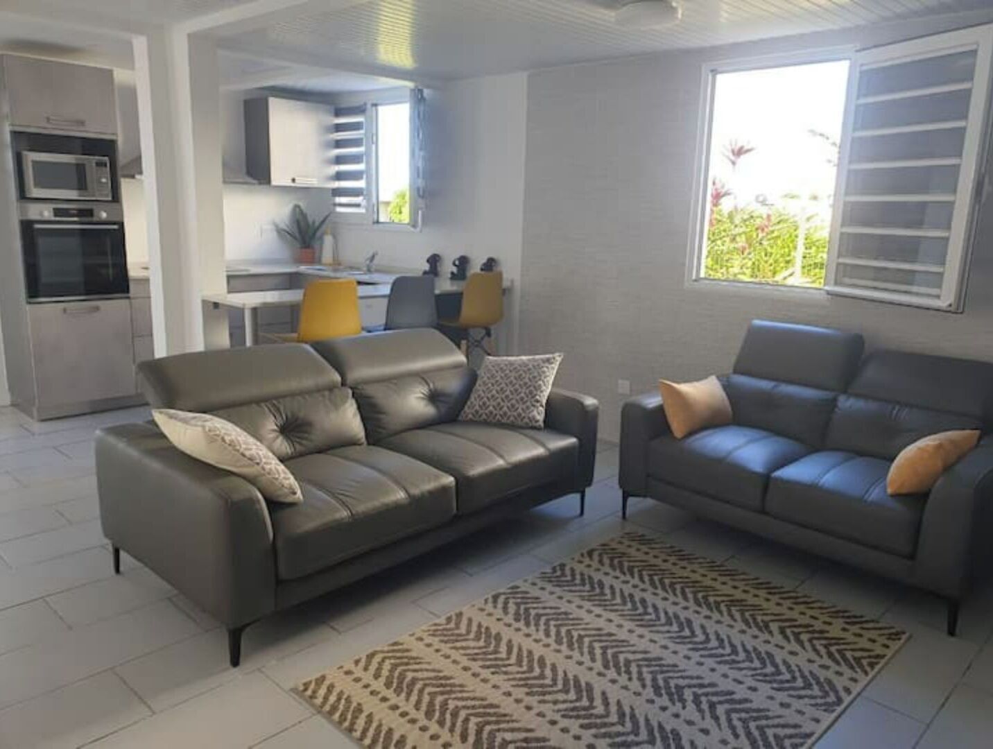 A modern living room with two sofas, a kitchen area, and a dining table.