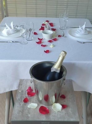 Une table dressée pour un repas, avec une bouteille de champagne dans un seau à glace, entourée de pétales de rose.