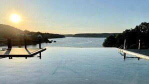 Une piscine extérieure paisible, dotée d’une terrasse en bois, entourée d’arbres et offrant une vue sur une étendue d’eau calme.