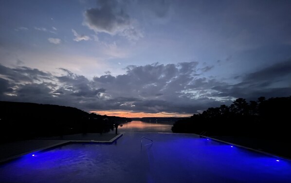 A swimming pool at dusk with a view of the sky and distant landscape.