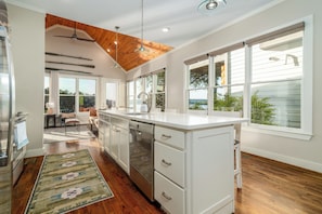 A modern kitchen with a large island, wooden ceiling, and large windows.