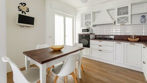 Una cocina moderna con armarios blancos, encimera de madera y una zona de comedor con sillas blancas.