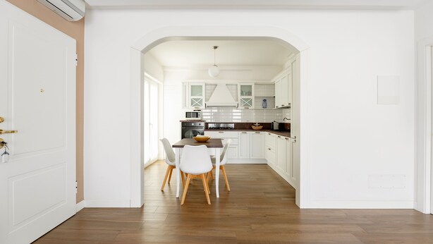 Una cocina moderna con armarios blancos, una mesa de comedor con sillas y suelo de madera.