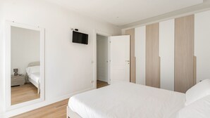 Un dormitorio con una cama grande, un armario, un espejo y un televisor en la pared.