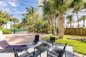 Eine Terrasse im Freien mit Liegestühlen und einem Tisch mit Glasplatte, umgeben von Palmen und einem Ziegelweg.
