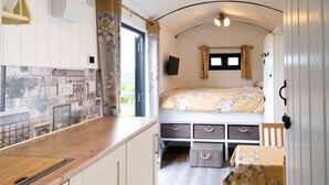 A compact RV interior with a kitchenette, a bed, and a small dining area. - Shepherd's hut with hot tub (Bodmin)