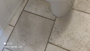 Et toilet med hvidt sæde og låg, en hvid væg med et sort bogstav 'N' og et flisegulv.