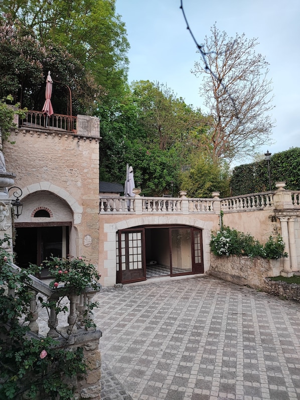 A courtyard with a stone pathway, a statue, and a building with arched windows and a balcony.
