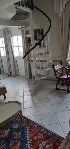 Una escalera de caracol en una habitación con un tapete estampado, una silla de madera y un radiador blanco.