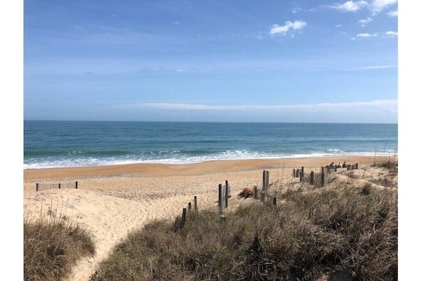 A beach with a wooden fence and dunes in the foreground.