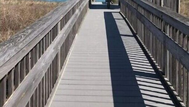 Ein hölzerner Steg führt zu einem Gazebo mit einem Reetdach, mit Blick auf einen Strand.