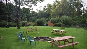Ein Garten mit Schaukel, Picknicktischen und Feuerstelle.