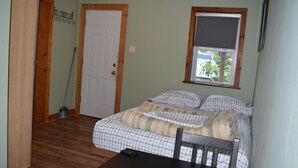 Ein Schlafzimmer mit einem Bett, einem Fenster mit Jalousie, einer Tür und einem an der Wand angelehnten Besen.