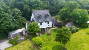 A large, two-story house with a sloped roof, surrounded by lush greenery and trees. - Charming Guest House in Cornish countryside - Demelza Cottage (BODMIN)