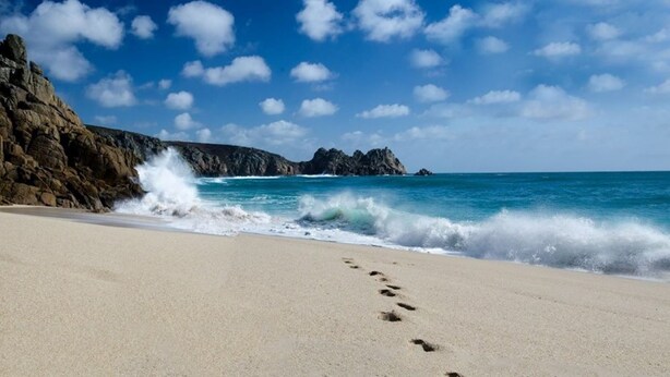 A sandy beach with footprints leading to the water, rocky cliffs, and a clear blue sky. - Charming Guest House in Cornish countryside - Demelza Cottage (BODMIN)
