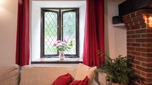 A cozy living room with a beige sofa, a red throw pillow, a vase with flowers, and a brick fireplace. - Charming Guest House in Cornish countryside - Demelza Cottage (BODMIN)