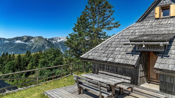 Une cabane en bois avec une enseigne indiquant « ZLATOROG » et une terrasse en bois dotée de bancs.
