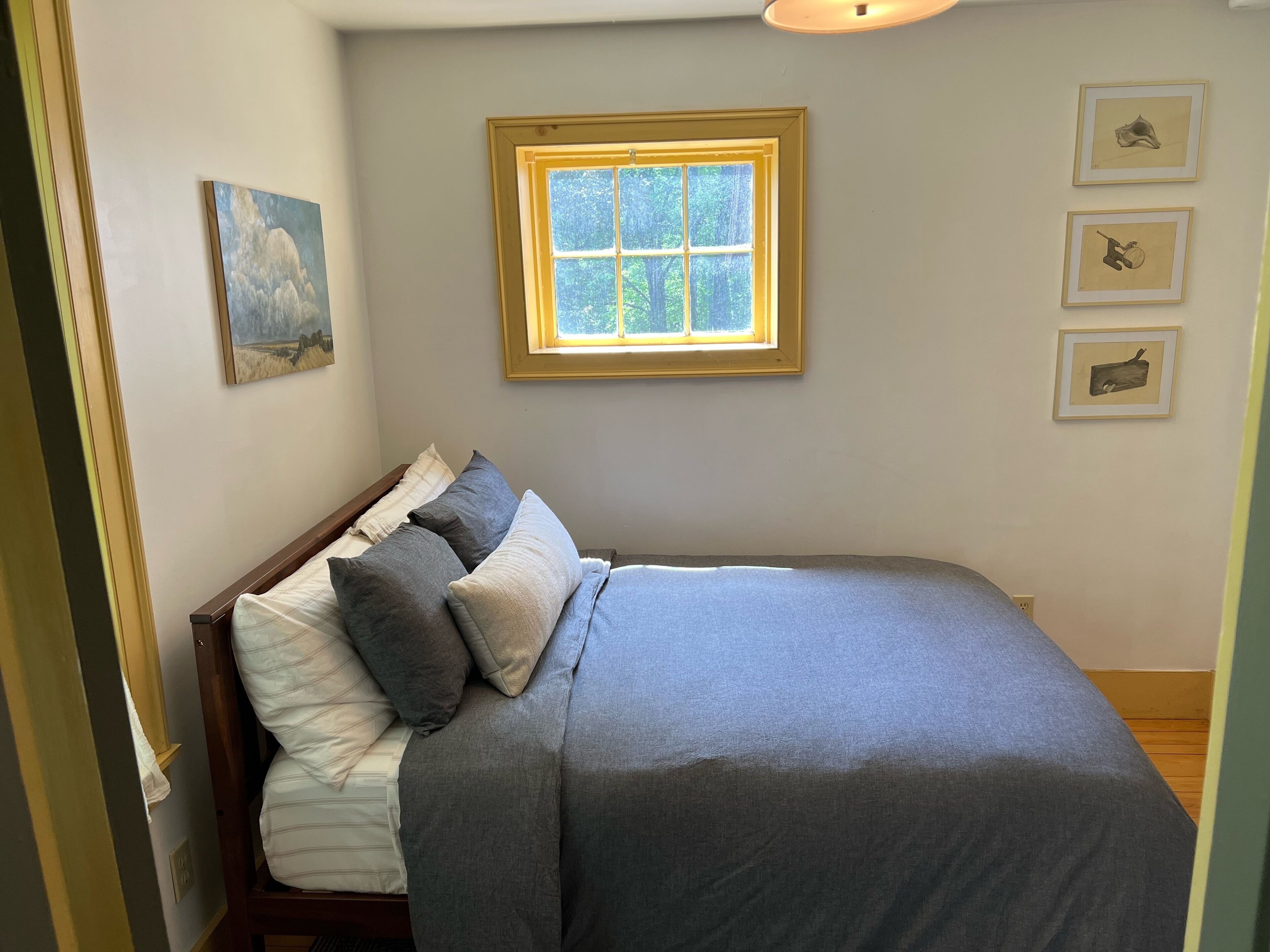 Un dormitorio con una cama, un ventanal y tres cuadros en la pared.