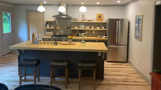 Een moderne keuken met een centraal eiland, barstoelen, hanglampen, een koelkast en een betegelde spatwand.