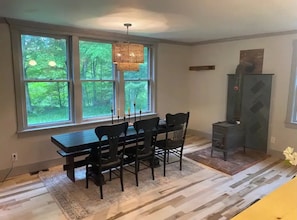 Un comedor con una mesa y sillas, ventanas amplias con vistas a zonas verdes, una lámpara colgante y una chimenea.
