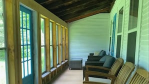 Een overdekt terras met houten stoelen en banken, grote ramen en een houten plafond.