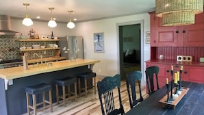 Een moderne keuken met een centraal kookeiland, barstoelen en een eethoek met een zwarte tafel en stoelen.