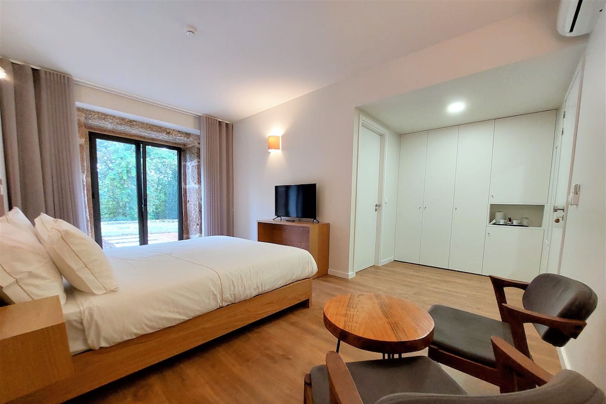 A modern hotel room with a bed, a TV, a seating area, and a wardrobe.