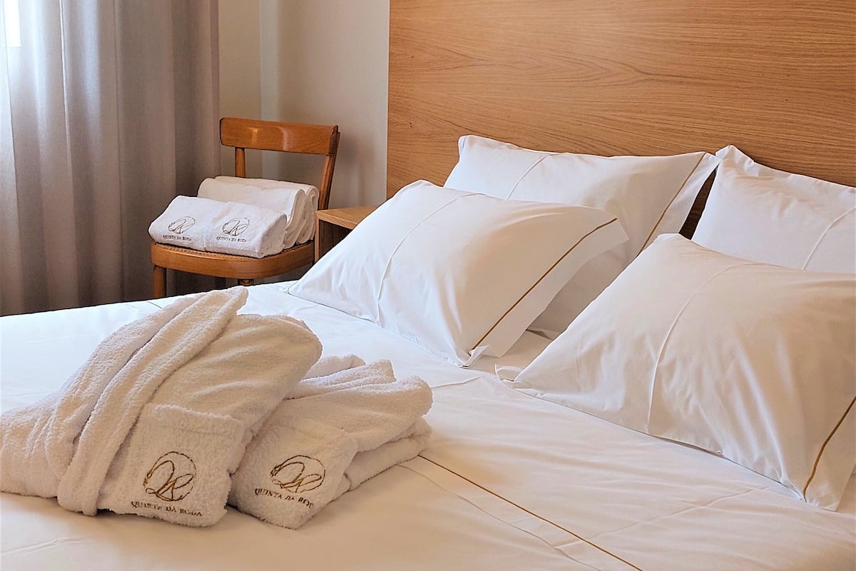 A neatly made bed with white linens and two towels with embroidered text.