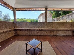 A covered outdoor seating area with a stone bench and a small table, overlooking a stone wall and greenery. - Quinta da Roda - Nature and Wellness (Vila Verde)