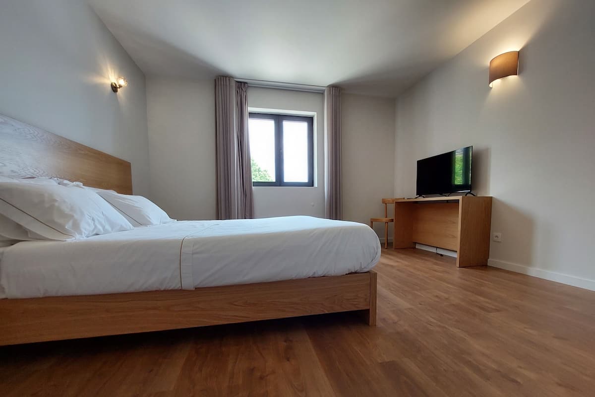 A bedroom with a wooden bed, a TV on a wooden stand, and a window with curtains.