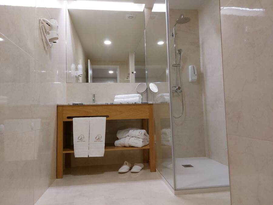 A modern bathroom with a glass-enclosed shower, a wooden vanity, and a shelf with towels and slippers.