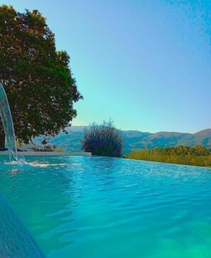 A swimming pool with clear blue water, surrounded by greenery and mountains in the background. - Quinta da Roda - Nature and Wellness (Vila Verde)
