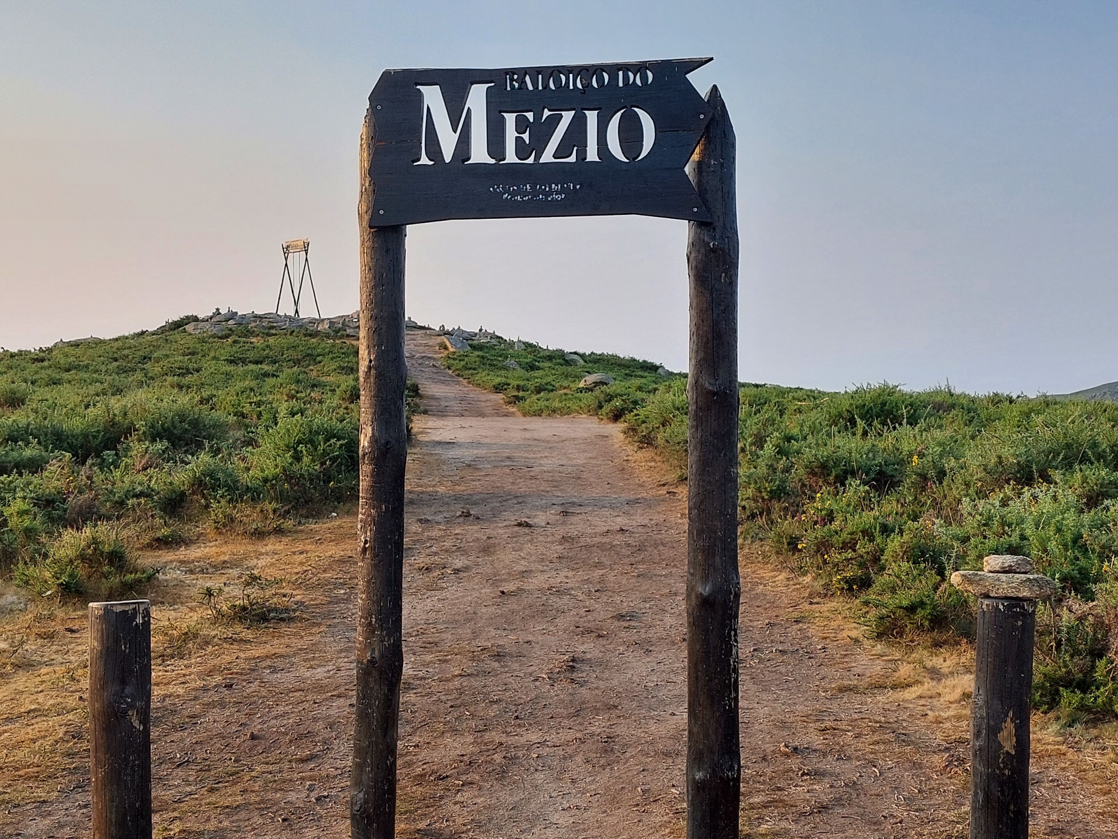 A dirt path leading to a sign that reads "Baile do Meio."