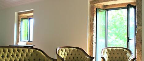 A room with a green sofa and two armchairs, a table, and a large window with a view of greenery.