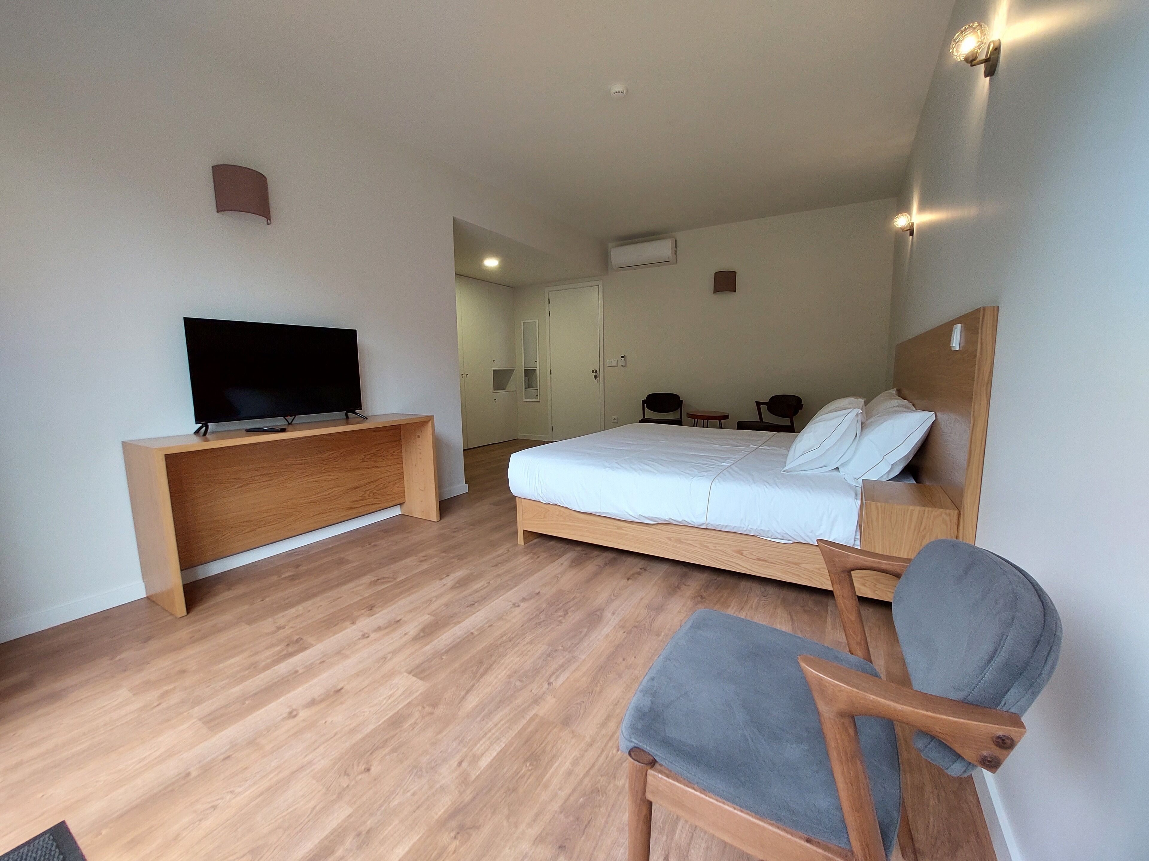 A hotel room with a bed, a TV on a wooden desk, a chair, and a small table.