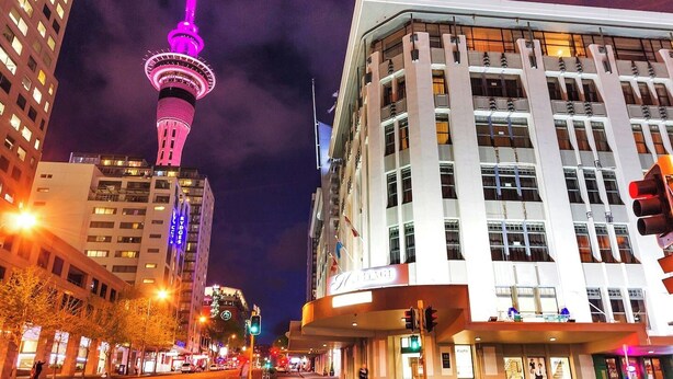 Un paisaje urbano con una torre destacada iluminada en rosa, edificios modernos y un semáforo.