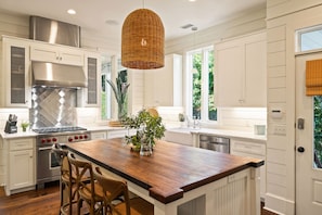 A kitchen with white cabinetry, a large wooden island, stainless steel appliances, and a hanging wicker light fixture.
