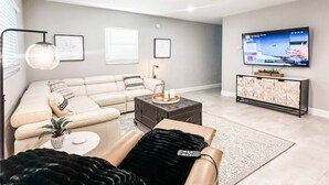 A modern living room with a sectional sofa, a coffee table, and a flat-screen TV mounted on the wall. - Super close to the beach. Private Hot Tub Backyard (Naples)
