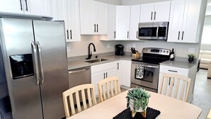 A modern kitchen with white cabinets, stainless steel appliances, a dining table with chairs, and a potted plant. - Super close to the beach. Private Hot Tub Backyard (Naples)