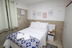A neatly made bed with a patterned bedspread, a bedside table with a lamp and flowers, and a wall with framed artwork.