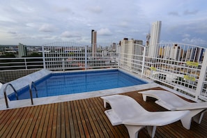 Piscina no terraço com deck de madeira e espreguiçadeiras brancas.
