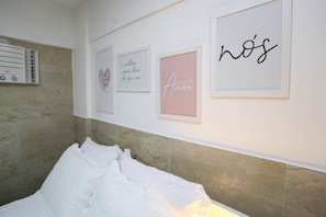 Quarto com cama, ar condicionado fixado na parede e três quadros emoldurados.