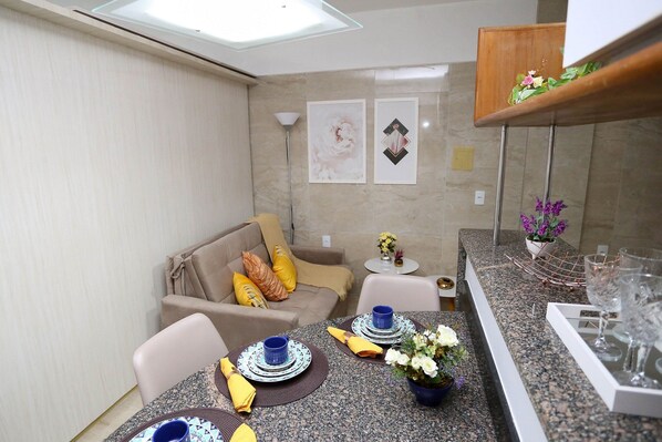 A compact living space with a dining area, a sofa, and a small side table with decorative items. - Incrível suíte em Manaíra por Carpediem (João Pessoa)