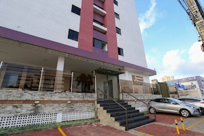 A multi-story building with a red and white facade, a visible staircase, and a parking area with cars.