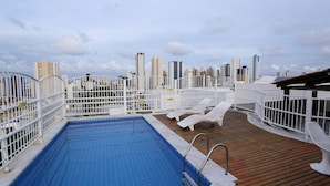 A rooftop pool with a city skyline view, white railings, and lounge chairs. - Incrível suíte em Manaíra por Carpediem (João Pessoa)