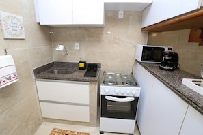 Cozinha compacta com armários brancos, bancada de granito, fogão a gás, micro-ondas e cafeteira.